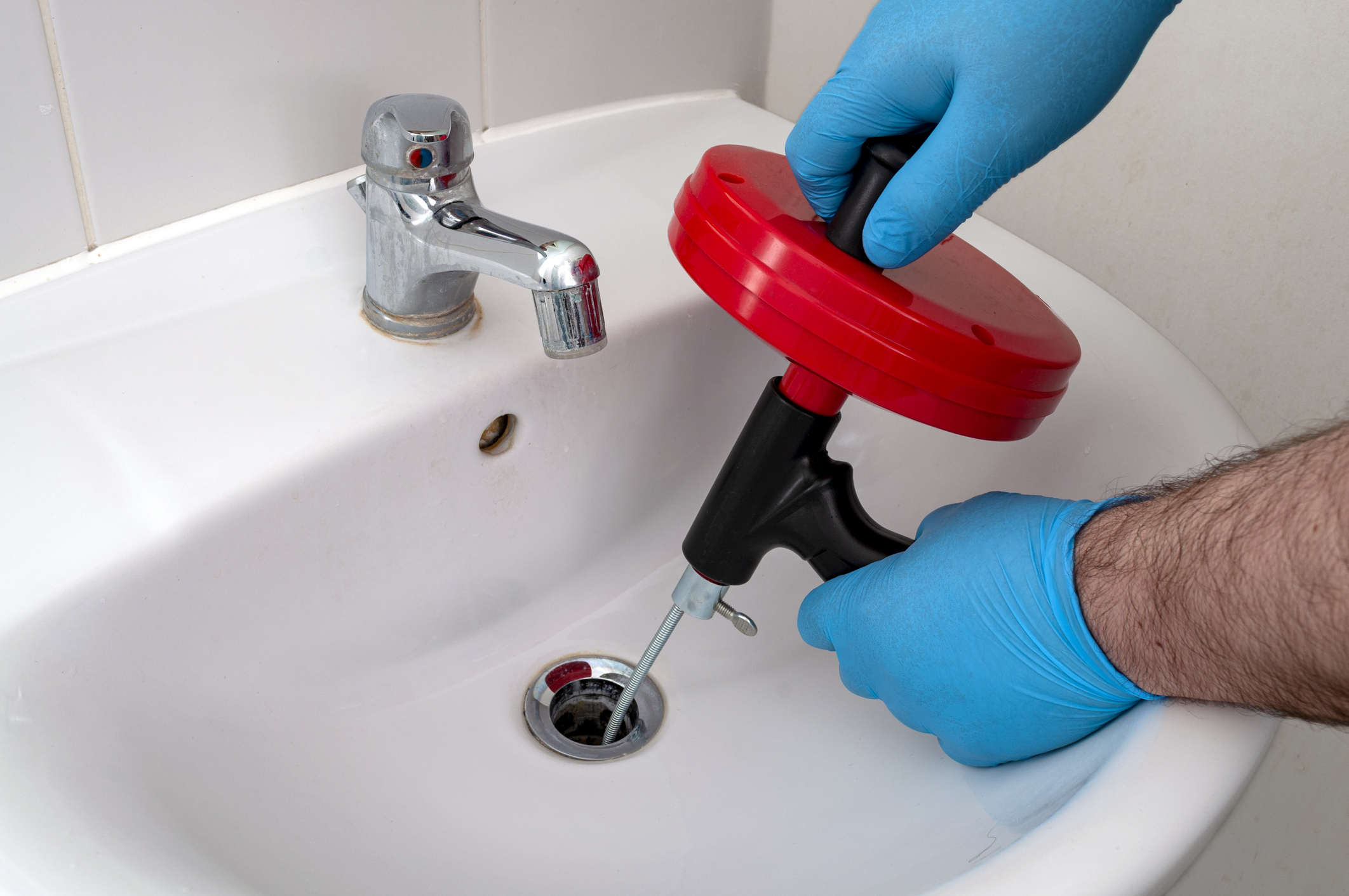 Plumber using drain snake down sink to unclog