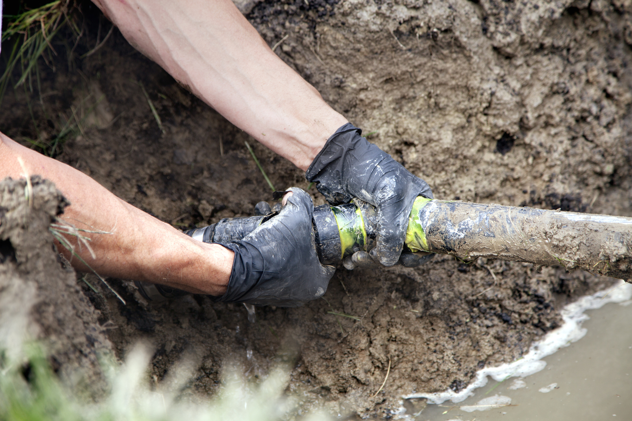  Plumbers hands on an outdoor sewer pipe in mud