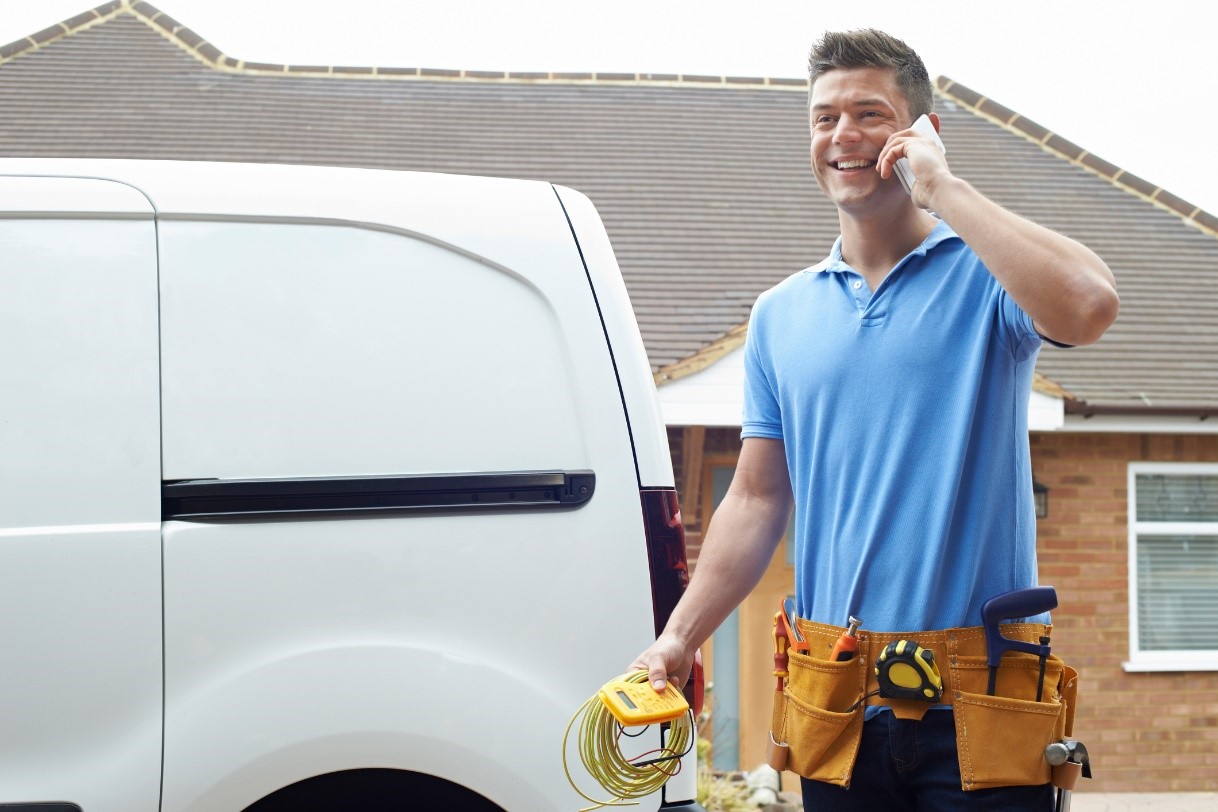 A technician wearing a tool belt and talking on the phone in front of a white work van